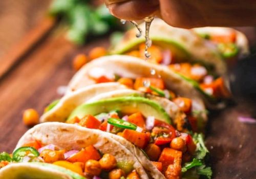 The image shows several tacos filled with chickpeas and vegetables on a wooden board, topped with fresh lime juice being squeezed over them.