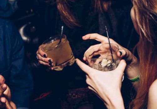 A close-up of people socializing, holding drinks in their hands, and appearing to be in a lively environment, perhaps a bar or a party.