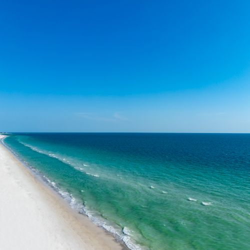 A wide sandy beach stretches along the turquoise ocean with gentle waves under a bright blue sky.