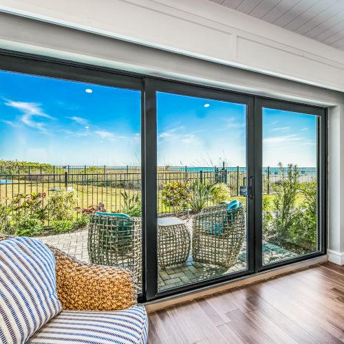 This image shows a bright room with a large sliding glass door leading to a patio with outdoor furniture and a scenic view of a blue sky and field.