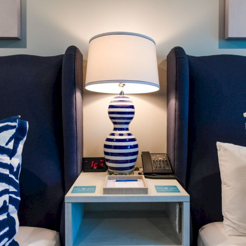 A bedside table with a blue and white striped lamp, flanked by two blue chairs and zebra print pillows, sits below two wall artworks.