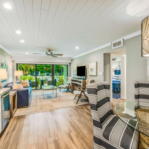 A modern living space with an open-plan kitchen, dining area, and living room, featuring stylish furniture and decor, and a view of greenery through large sliding doors.