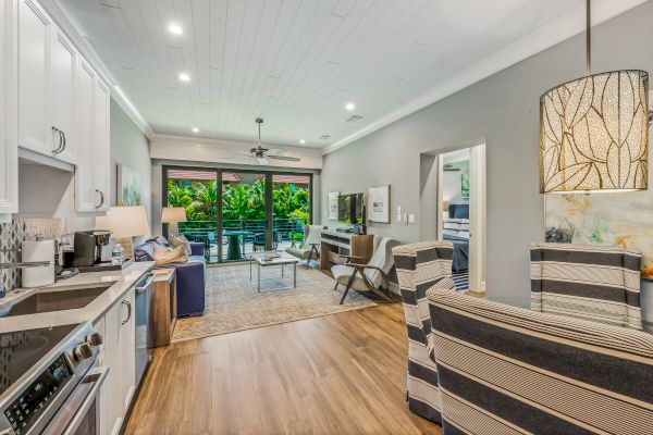 A modern open-plan living area with a kitchen, dining, and lounge space. The room features large sliding doors opening to a greenery-filled balcony.