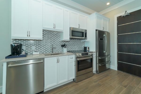 A modern kitchen with white cabinets, stainless steel appliances, gray tile backsplash, and wooden flooring.