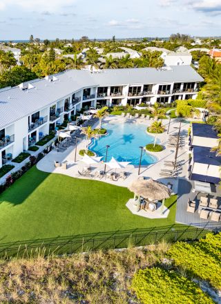 This image features a modern resort with a pool, multiple lounge areas, and well-maintained greenery, surrounded by other buildings and palm trees.