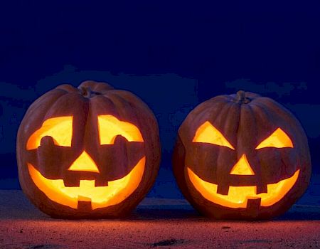 Two glowing carved pumpkins with smiling faces are set against a dark background, resembling classic Halloween jack-o'-lanterns.