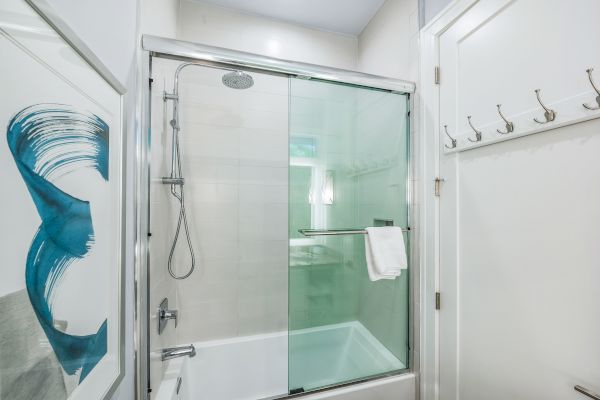 A modern bathroom features a glass-enclosed shower with a towel, abstract artwork on the wall, and multiple hooks on the door.