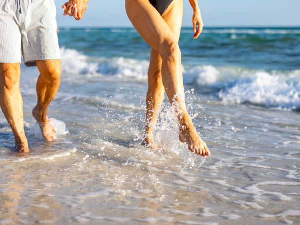 Two people walking along a sunny beach, enjoying the water and waves.